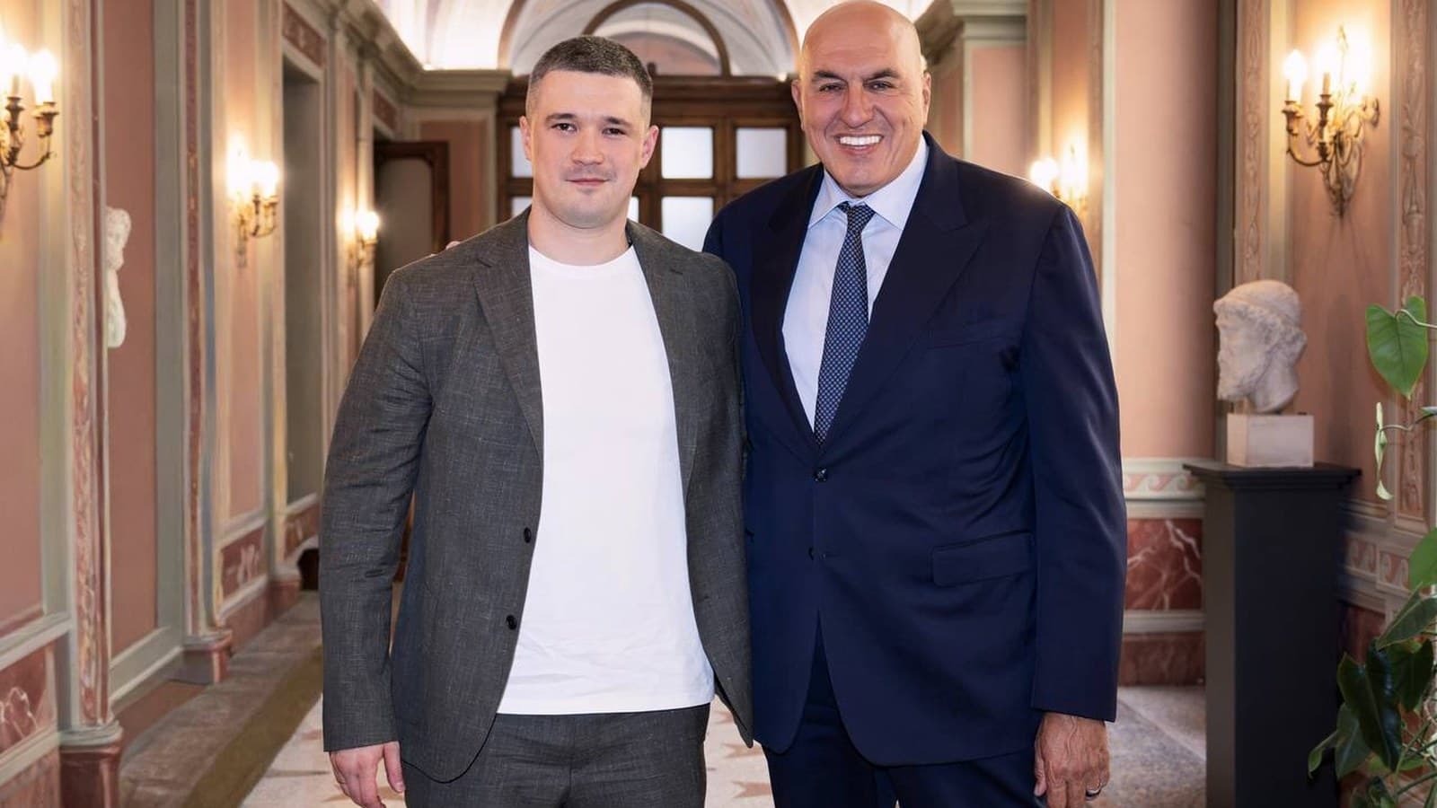 Mykhailo Fedorov e Guido Crosetto in piedi, sorridenti, in un corridoio affrescato di un palazzo italiano.