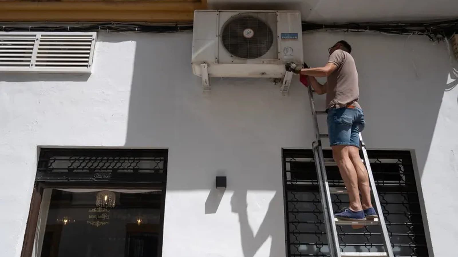 Un uomo su una scala installa un condizionatore sulla parete bianca di una casa.