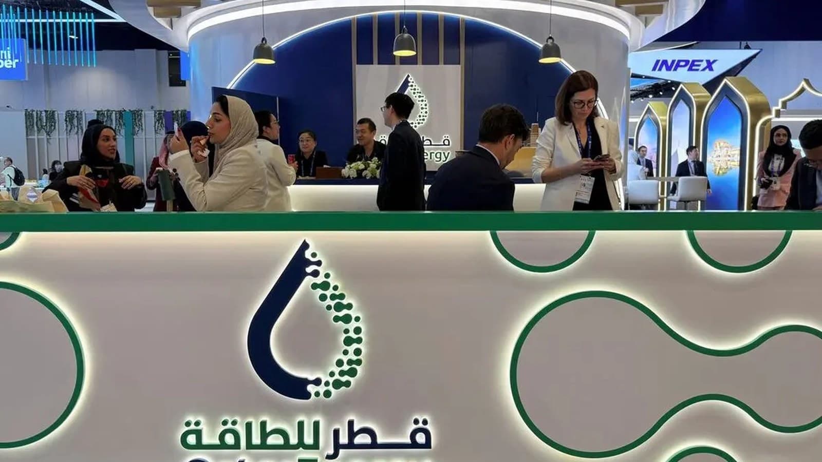 Alcune persone si radunano allo stand di QatarEnergy sotto il logo dell'azienda durante una conferenza di settore.
